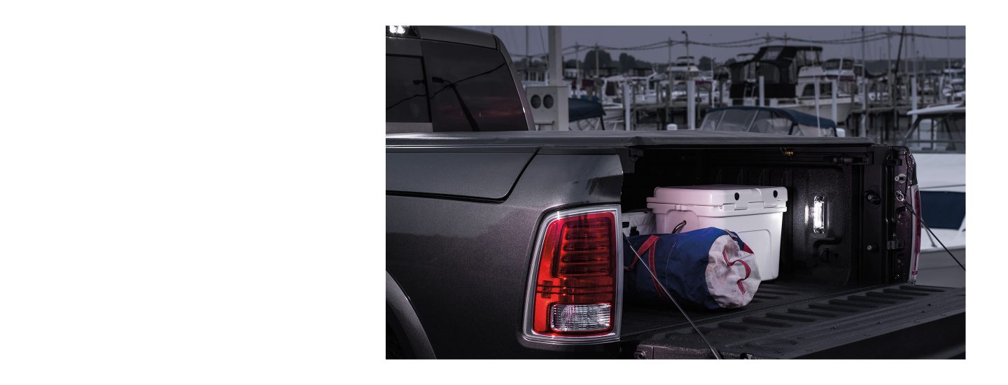 The bed of the 2022 Ram 1500 Classic with the tailgate down to reveal a cooler and duffel bag under the tonneau cover.